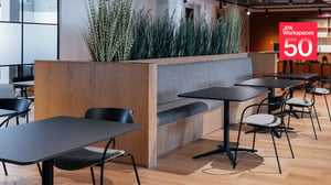 Planted banquette seating and cafe tables furnished by JPA Workspaces, with the JPA Workspaces 50 years badge